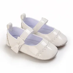 Close-up of white patent leather baby princess shoes with bow and decorative pattern