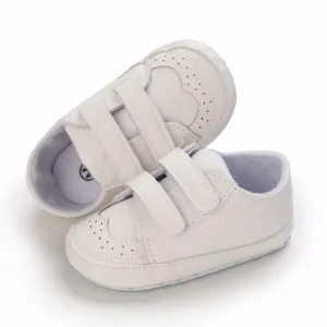 Close-up of white soft sole baby walking shoes with double Velcro straps and heart stitching.