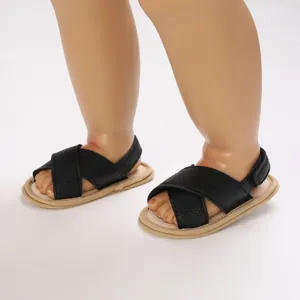 Primer plano de sandalias negras para bebé con tiras cruzadas y suela de tela suave