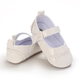 Close-up detail of white glossy baby Mary Jane shoes featuring a bow and scalloped edges