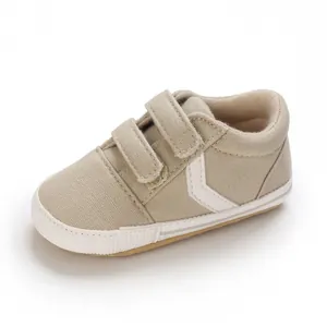 Vista detallada de una zapatilla de lona beige para bebé con doble cierre de velcro en blanco