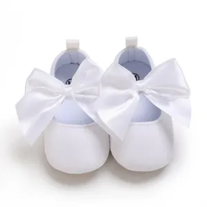 Vue détaillée de chaussures de princesse blanches pour bébé avec de grands nœuds en satin.