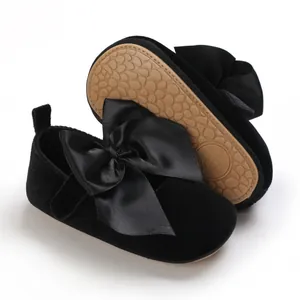 Primer plano de zapatos de princesa para bebé en terciopelo negro con un gran lazo de satén