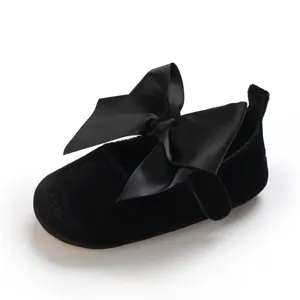 Détail d'une chaussure de princesse en velours noir pour bébé avec grand nœud.