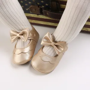 Nahaufnahme goldener Lauflernschuhe für Babys mit großer Schleife und weicher Sohle