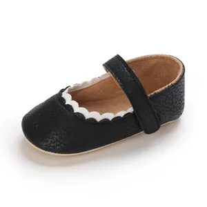 Nahaufnahme schwarzer Baby Mary Janes mit weißem Wellenrand und weicher Kieseltextur.