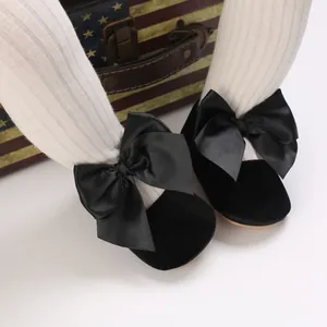 Gros plan de chaussures de princesse bébé en velours noir avec nœuds en satin sur bas