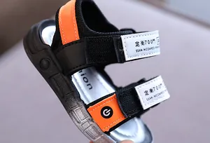 Detailaufnahme der schwarzen und orangefarbenen Jungensandalen mit Klettverschlussriemen.