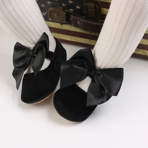 Gros plan de chaussures de bébé en velours noir avec nœuds et collants blancs côtelés.
