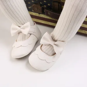 Nahaufnahme cremeweiße Baby-Prinzessinenschuhe zum Laufenlernen mit Schleife und Wellenrand