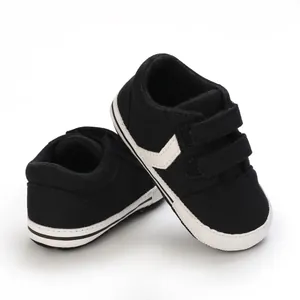 Zapatillas de lona negras para bebé con suelas blancas suaves y cierres de velcro.