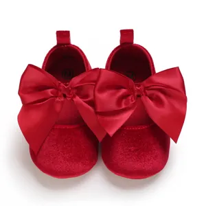 Détail de chaussures de princesse bébé en velours rouge avec grands nœuds en satin.
