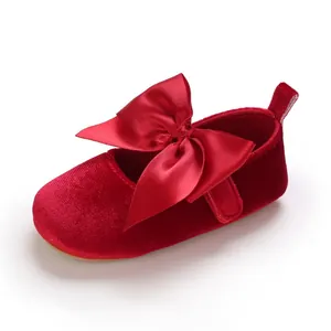 Gros plan d'une chaussure de bébé en velours rouge avec un grand nœud en satin