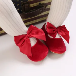 Gros plan de chaussures de princesse pour bébé en velours rouge avec un grand nœud en satin.