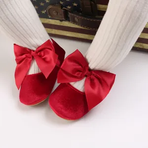 Détail de chaussures de princesse en velours rouge avec grands nœuds en satin pour bébés.
