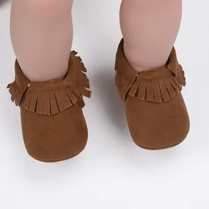 Detailansicht der braunen Wildleder-Babyschuhe mit Fransenbesatz an weichen Puppenfüßen.