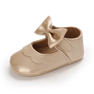 Nahaufnahme von einem goldenem Baby-Lauflernschuh mit Zierschleife und Wellenrand.
