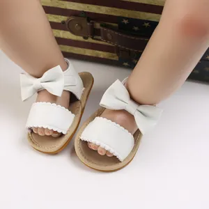 Dettaglio di sandali bianchi per neonata con fiocco decorativo e bordo smerlato