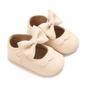 Close-up detail of cream baby walking shoes featuring a large bow and scalloped edges