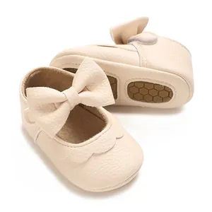 Detail view of cream baby girl princess shoes with large bow and scalloped edges.