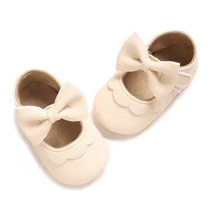 Close-up of beige baby girl walker shoes with large decorative bows and scalloped edges.