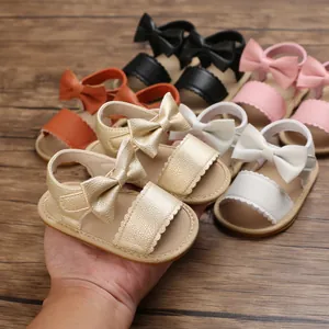 Dettaglio di sandali per neonata con fiocco decorativo e bordi smerlati in oro e bianco