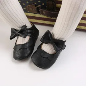Detailed view of black baby girl princess shoes featuring large bows and scalloped edges