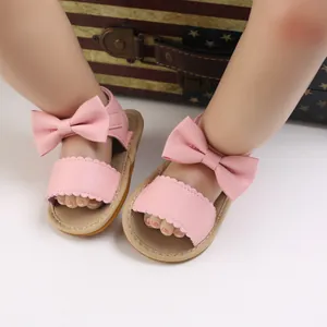 Primo piano di sandali rosa per neonata con grande fiocco e bordo smerlato.