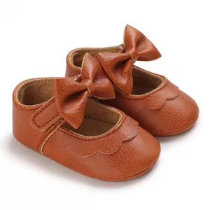 Detail von braunen Baby-Prinzessinenschuhen aus Leder mit großer Schleife und Wellenrand.