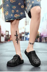 Detailed shot of black casual clogs worn with sunflower print denim shorts on street
