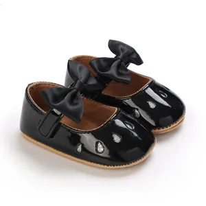 Primer plano de zapatos de charol negro para bebé niña con lazo y detalles brillantes.