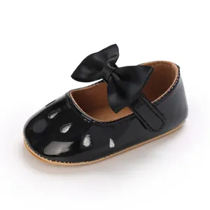 Detalle de zapato de bebé en charol negro con lazo de satén grande y recortes de purpurina