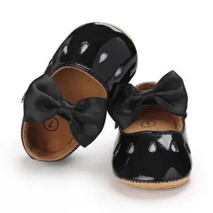 Detalle de zapatos de bebé niña en charol negro con lazo grande y gotas de purpurina