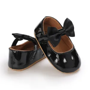 Detalle de zapatos de bebé niña en charol negro con lazo grande y suela blanda flexible