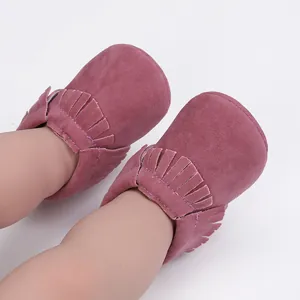 Nahaufnahme von altrosa Baby-Mokassins mit Fransendetail, die von einem Baby getragen werden