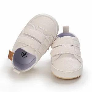 Detail of white soft-soled baby walking shoes featuring textured faux leather and straps.
