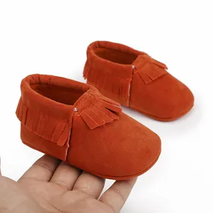 Detailansicht von weichen orangefarbenen Baby-Mokassins mit Fransen, Lauflernschuhe.