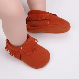 Nahaufnahme von leuchtend orangefarbenen Wildleder-Babyschuhen mit Fransen an einem Säugling