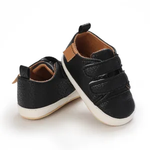 Close-up of black faux leather baby walking shoes with soft white soles and velcro straps.