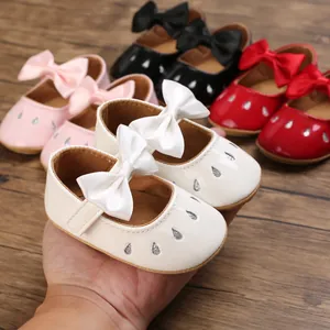 Primer plano de zapatos de bebé para niña blancos con lazo de satén y detalles brillantes.
