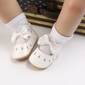 Vista detallada de zapatos blancos para bebé niña con suela de goma y adorno de lazo.