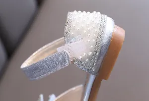 Κοντινό πλάνο με ασημί glitter, πέρλες και στρασάκια στο λουράκι του κοριτσίστικου παπουτσιού