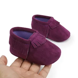 Detailansicht von lila Wildleder-Babyschuhen mit Fransen, die zur Größenmessung in der Hand liegen.