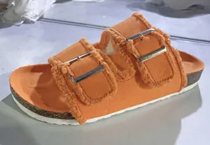 Close-up of stylish orange canvas slide sandals with frayed edges and double buckles