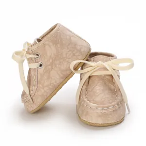 Nahaufnahme hellbrauner Leder Babyschuhe mit cremefarbenen Schleifen und weicher Sohle