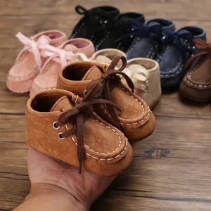 Nahaufnahme von braunen Baby-Lernschuhen aus Kunstleder mit weißen Nähten in der Hand.