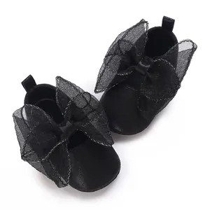 Draufsicht auf schwarze Babyschuhe mit übergroßen Netzschleifen auf weißem Grund