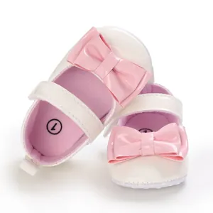 Detailaufnahme cremefarbener Babyschuhe mit rosa Schleifen und Antirutschsohle.