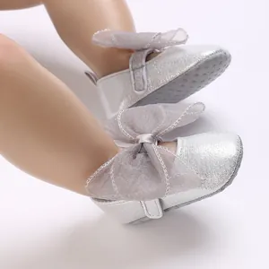 Detail von silbernen glitzernden Babyschuhen mit großer grauer Netzschleife.