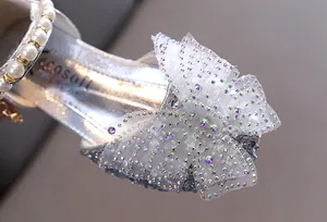 Primer plano del detalle de mariposa con diamantes en zapato plateado de princesa para niña.